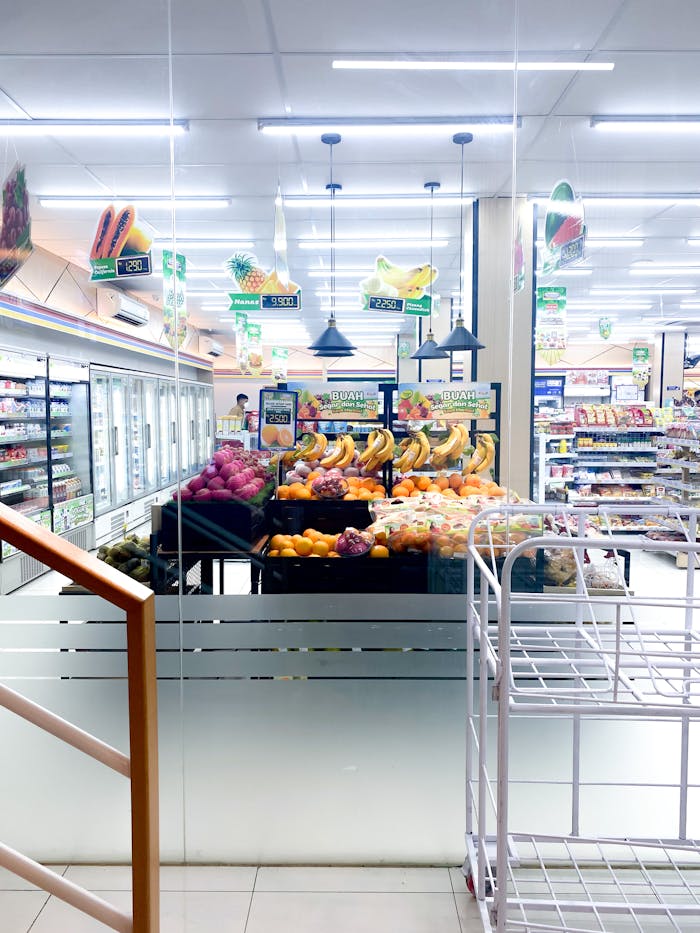 who-we-are Vibrant fruit display in a well-lit supermarket aisle with fridges and shelves.
